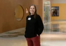 Professional woman in black sweater and burgundy pants smiling in modern office hallway