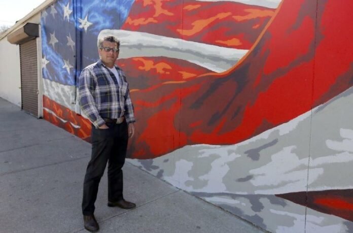 Scott LoBaido artist posing beside his American flag mural artwork