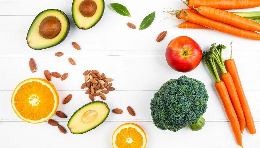 Fresh foods rich in fitosterina, such as avocados, oranges, broccoli, and carrots, displayed on a white surface.
